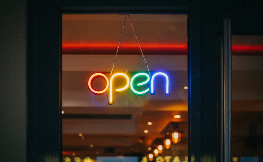 window with a multi coloured flourescent sign hanging in it saying open.