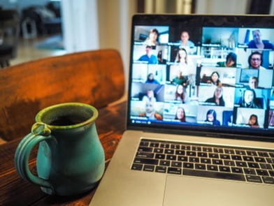 Open laptop with gallery view of online meeting participants, on a desk next to a pottery cup