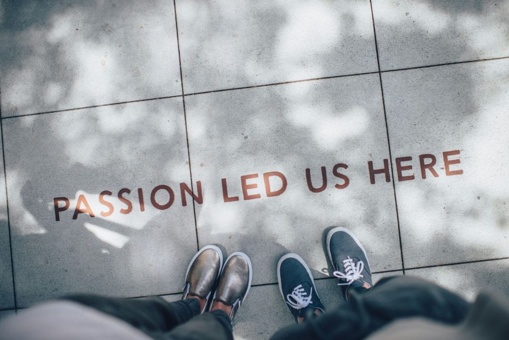 Two pairs of feet in shoes are visible on a footpath where it says Passion led us here