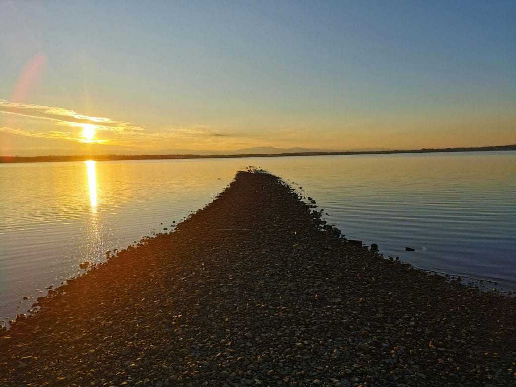 A road of pebbles leading into a sea or lake at sunset